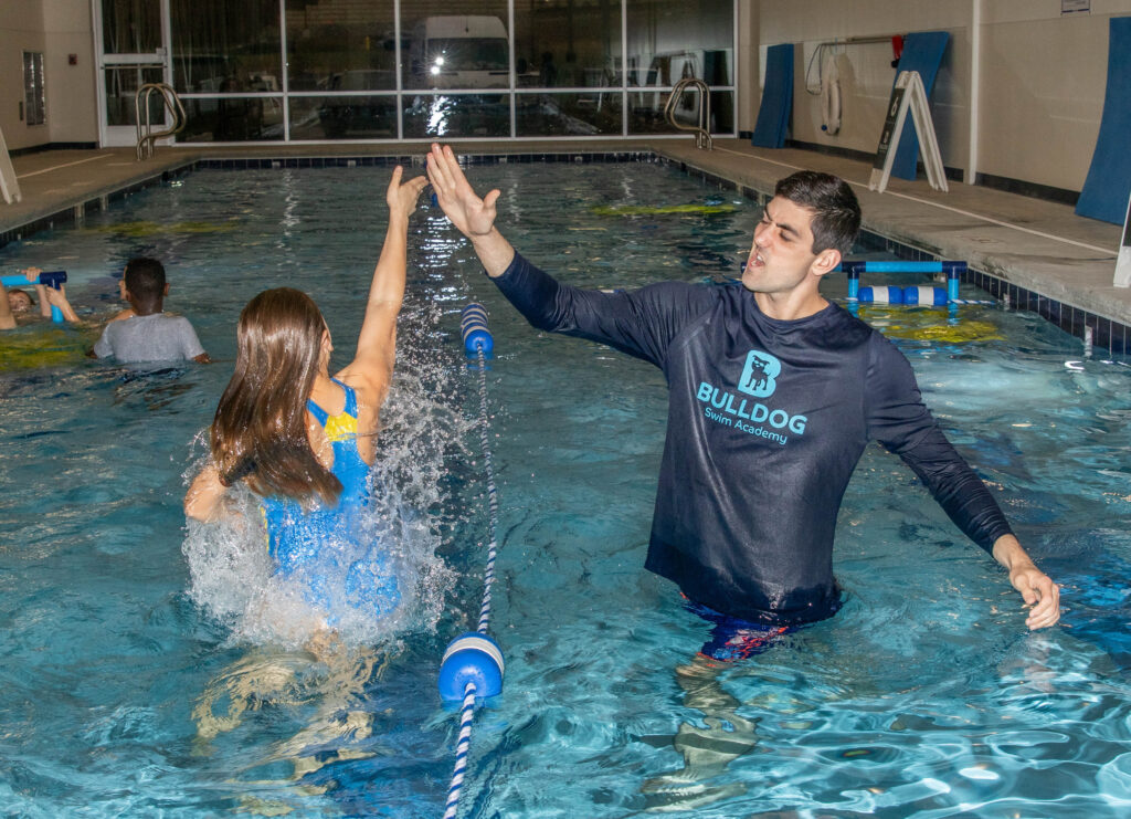 Swim instructor and student high-fiving in the pool